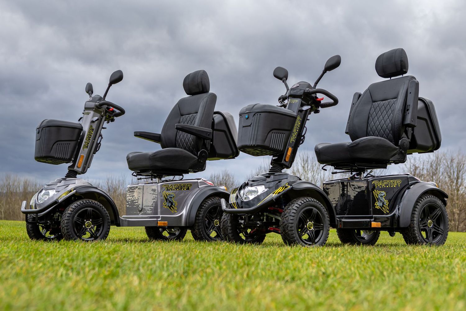 Three black and gray mobility scooters with padded seats parked on green grass under cloudy sky.