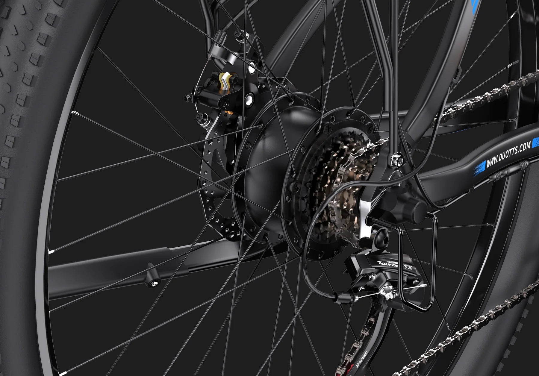 Close-up view of a bicycle’s rear wheel, showing the gears, derailleur, and disc brake system against a dark background. The black spokes and mechanical parts are prominently detailed.