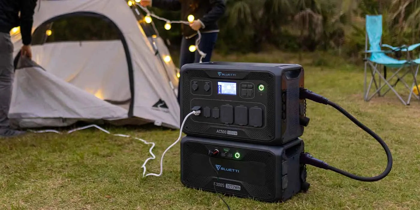Black portable power station connected to devices outside a tent at a campsite during dusk.