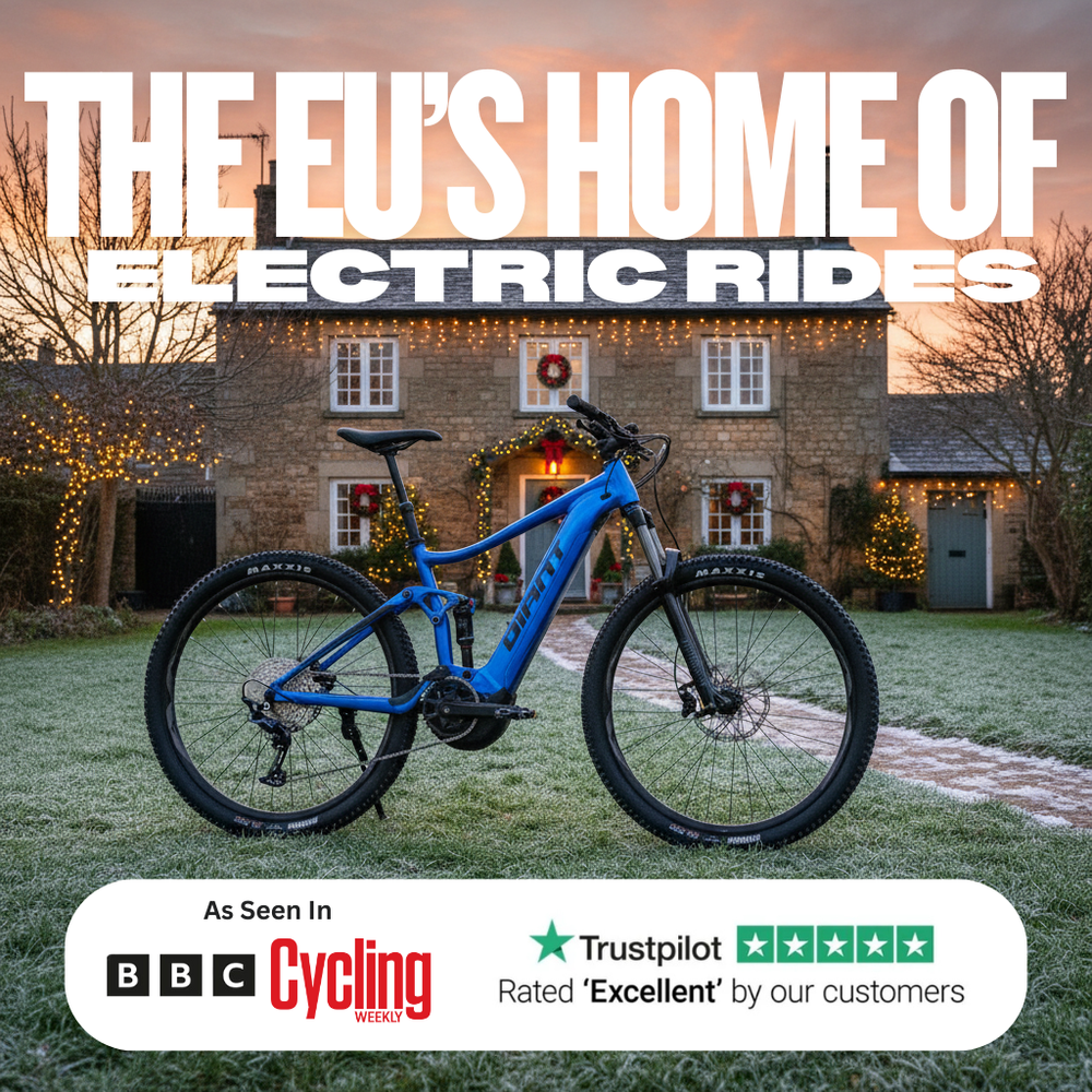 Blue electric mountain bike parked on frosty grass in front of a stone house decorated with Christmas lights at sunset