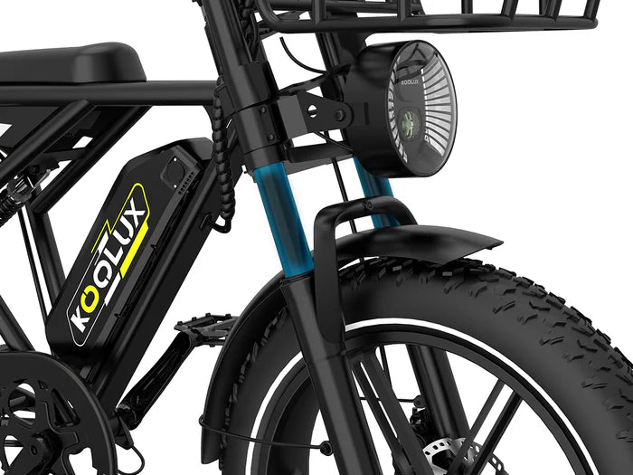 Close-up of the front section of a black Koolux electric bike, showing the headlight, thick front tire, fender, battery, and part of the bike frame with a front basket.