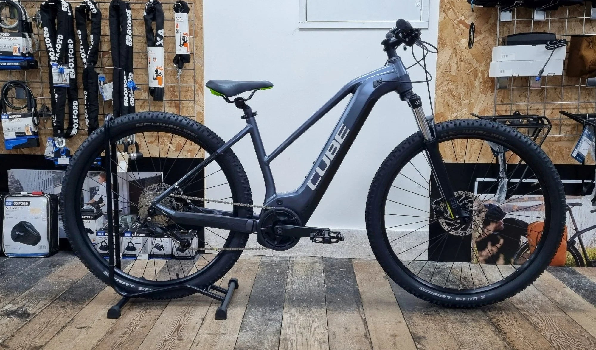Side view of a gray Cube electric mountain bike with black tires on a wooden floor inside a bike shop.