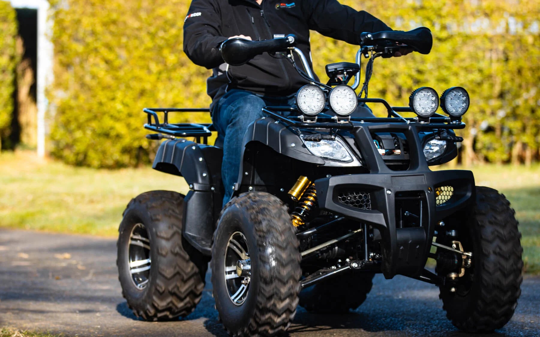 Person wearing dark clothing riding a black all-terrain vehicle (ATV) on a paved path outdoors