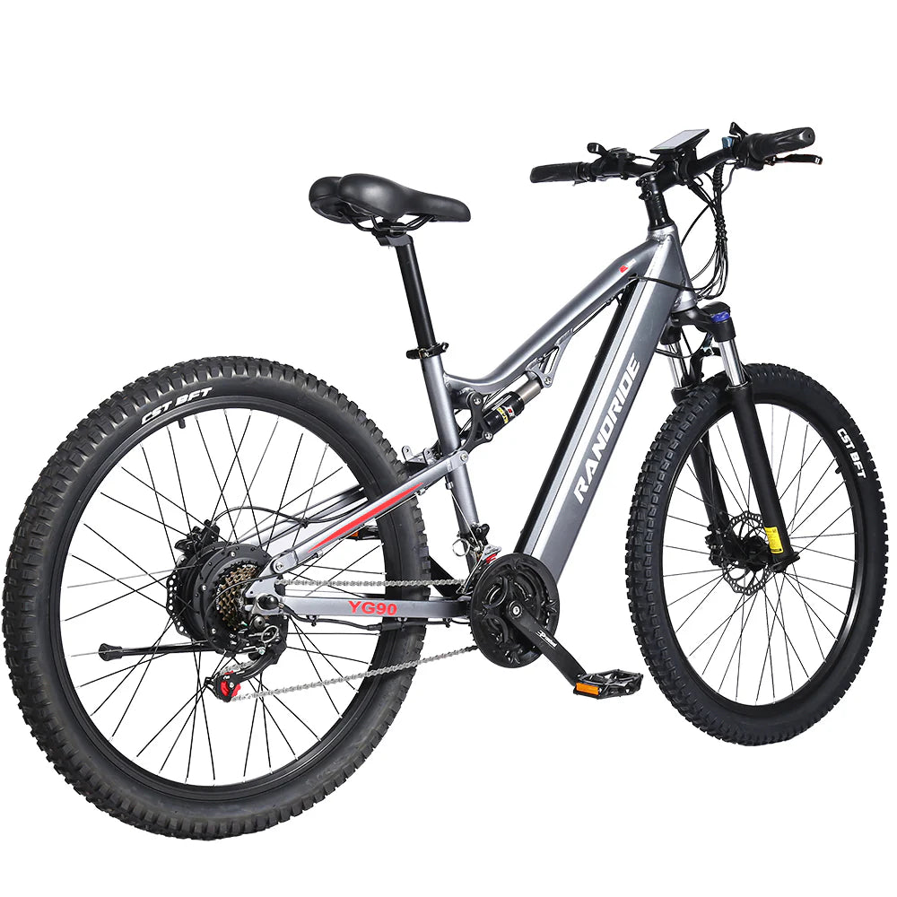 The Randride YX90A Electric Mountain Bike by Randride features a silver frame, 1000W rear hub motor, thick knobby tires, front suspension fork, black handlebars and seat. Shown from the rear left side on a white background.