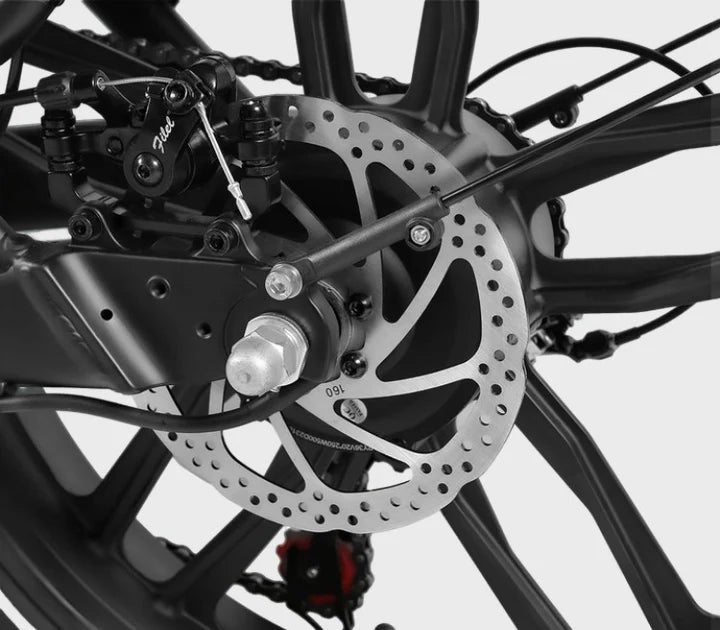Close-up of a bicycle’s rear wheel, showing the disc brake system, including the brake caliper, metal rotor, and spokes, with a black and silver color scheme on a light background.