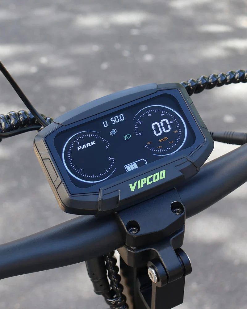 Close-up of the VIPCOO VS6 1000W Electric Scooter's digital display showing speed, battery, and other info on the handlebars with a blurred paved background. The Vipcoo brand name appears below the screen.