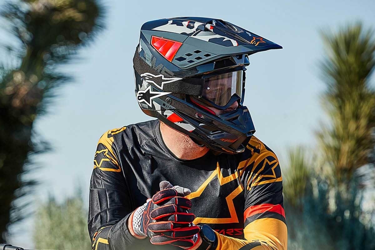 Person wearing a black, yellow, and red motocross outfit with a matching helmet and goggles outdoors with blurred trees in background